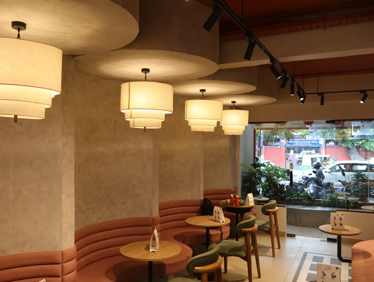 Warm pendant lights above curved coral seating inside Kora.Blr